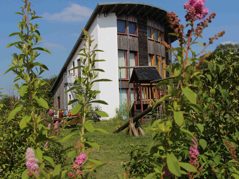 Sonniges Foto eines der Häuser der Siedlung in Neumühlen, im Vordergrund sind Blumen.